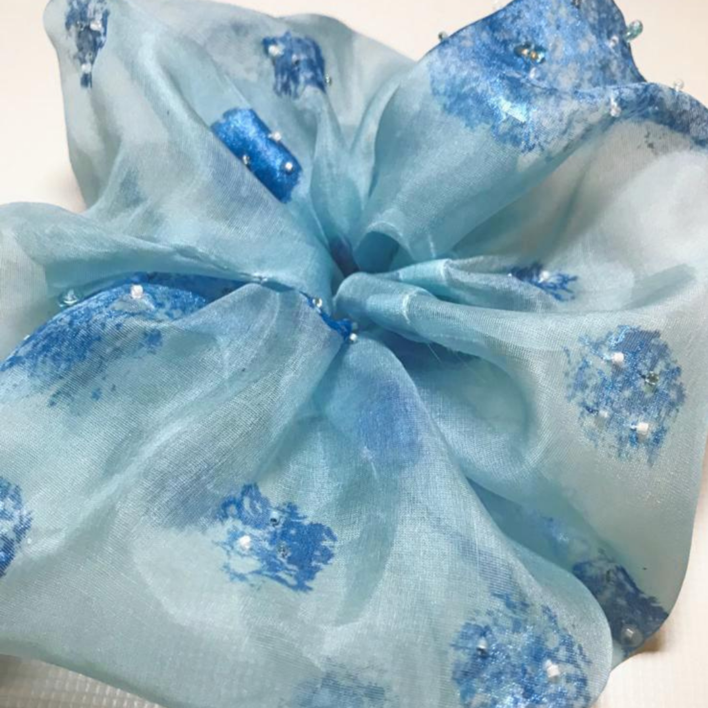 Scrunchy with blue fabric with floral patterns and embellishments on a white background