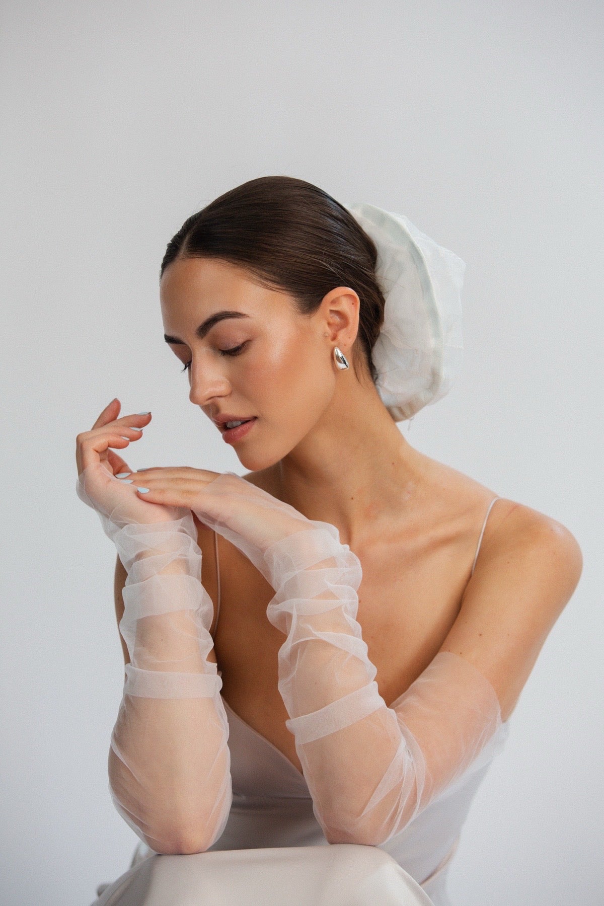 Bride wearing a white dress, veil, and gloves against a plain background