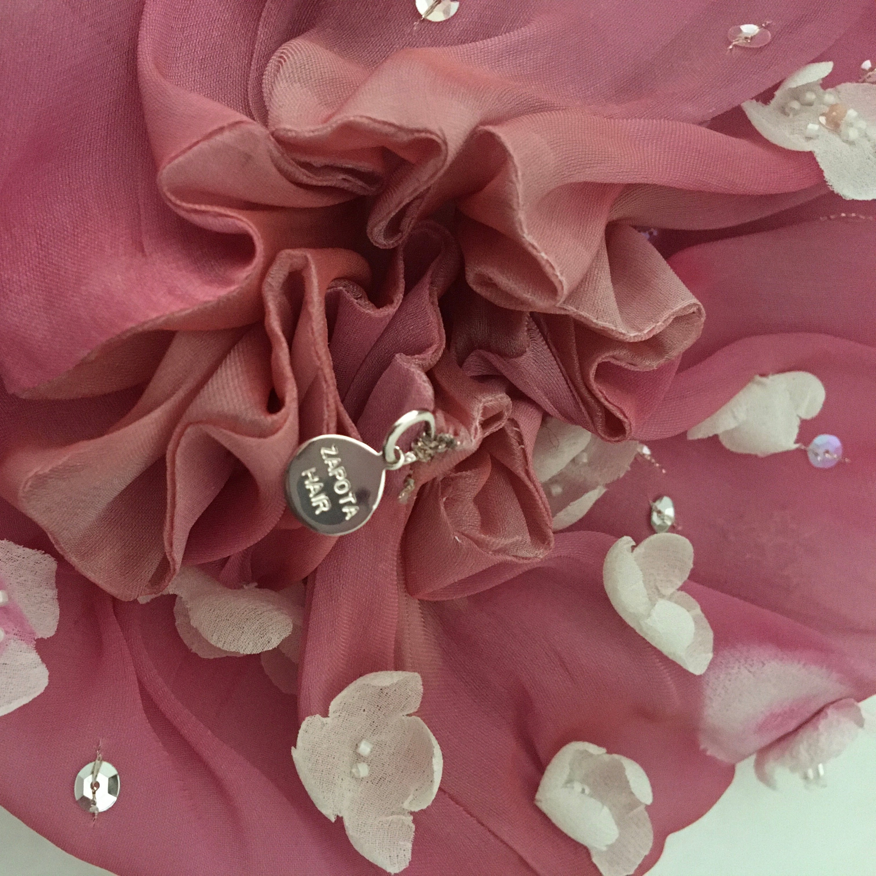Pink fabric with silk flowers and Zapota Hair brand tag on a light pink background