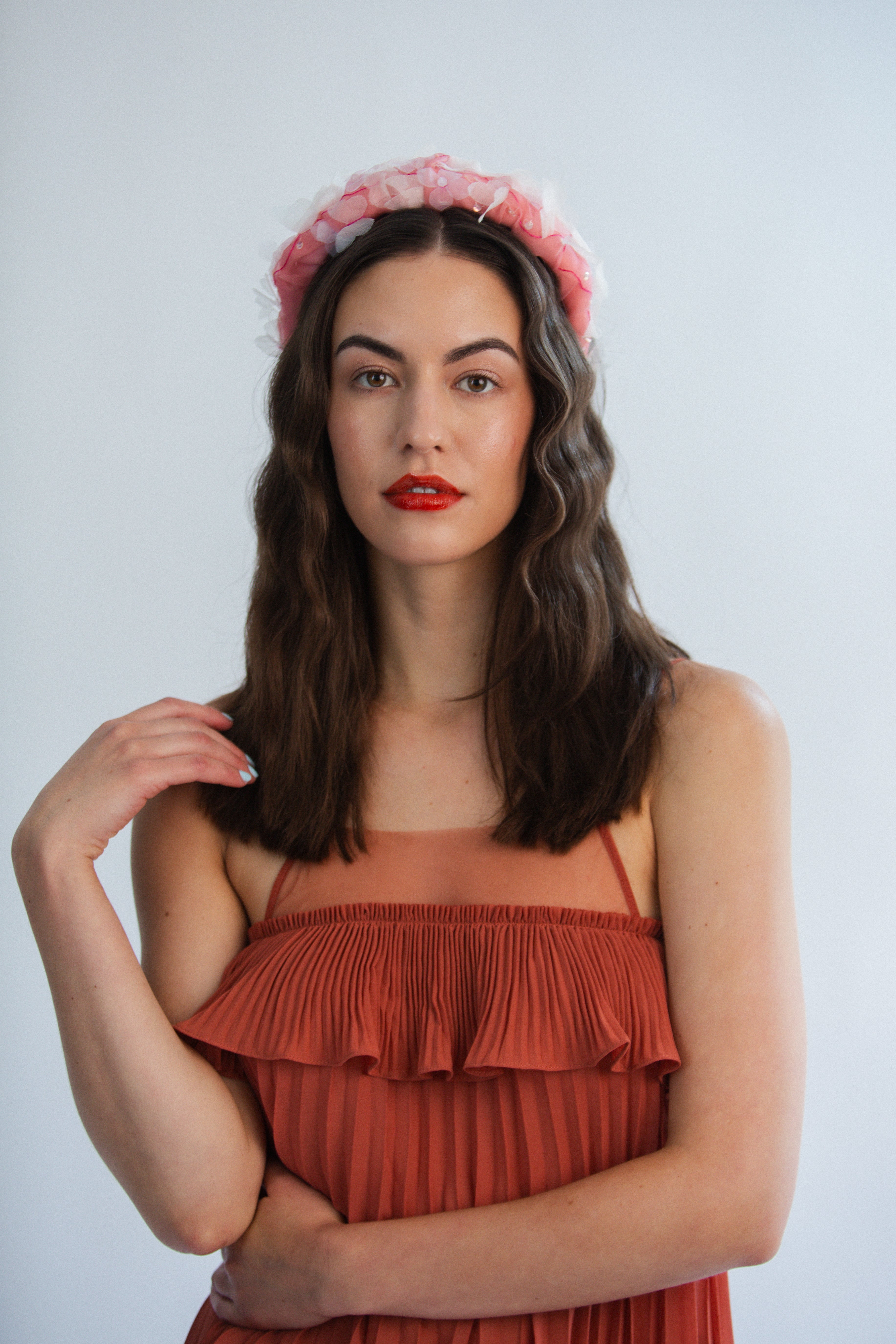 Woman wearing a rust-colored dress and pink floral headband against a light gray background