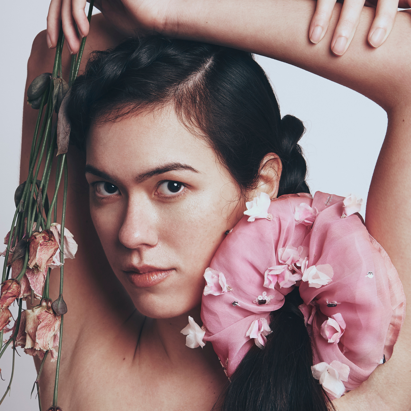 Woman with floral scrunchy and dried flowers, against a plain background