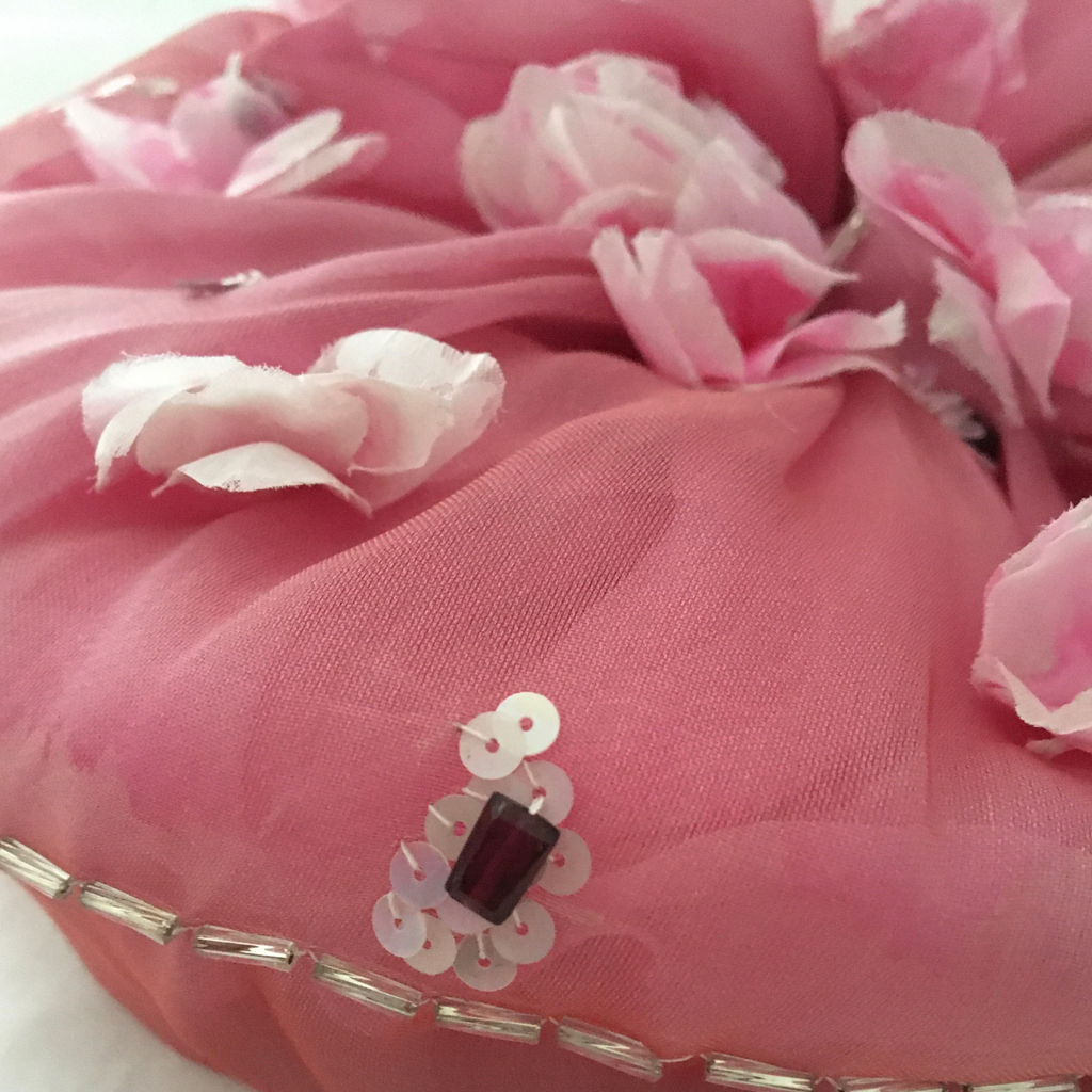 Pink fabric with floral embellishments and a decorative button on a white background