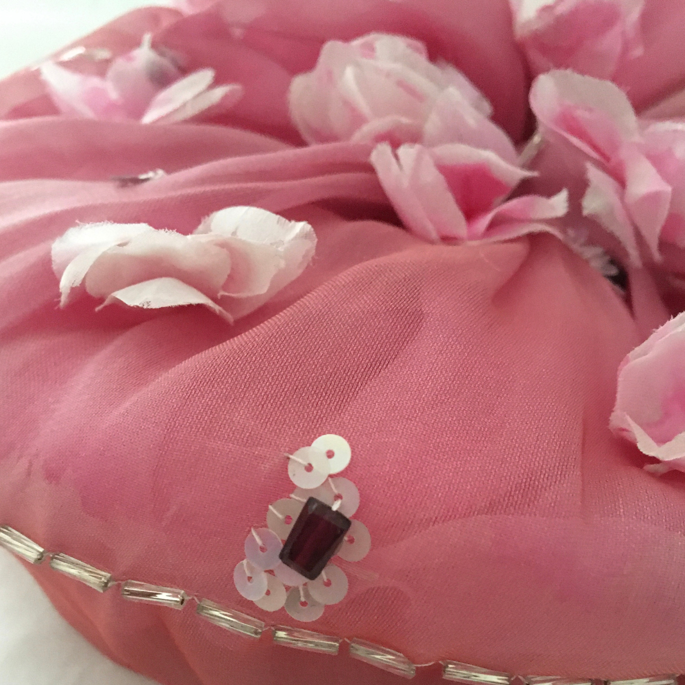 Pink fabric with floral embellishments and a decorative button on a white background
