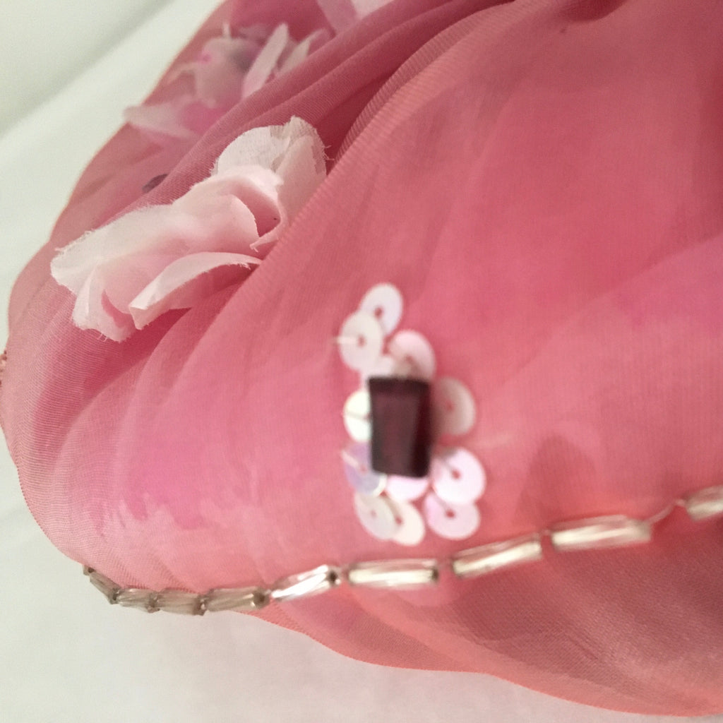 Close-up of a pink fabric scrunchy with decorative elements and gemtones on a white background