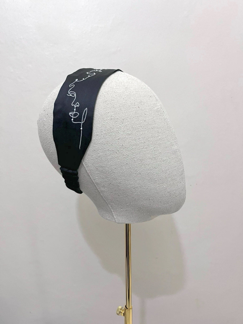Black headband with white text on a gray mannequin head against a white background