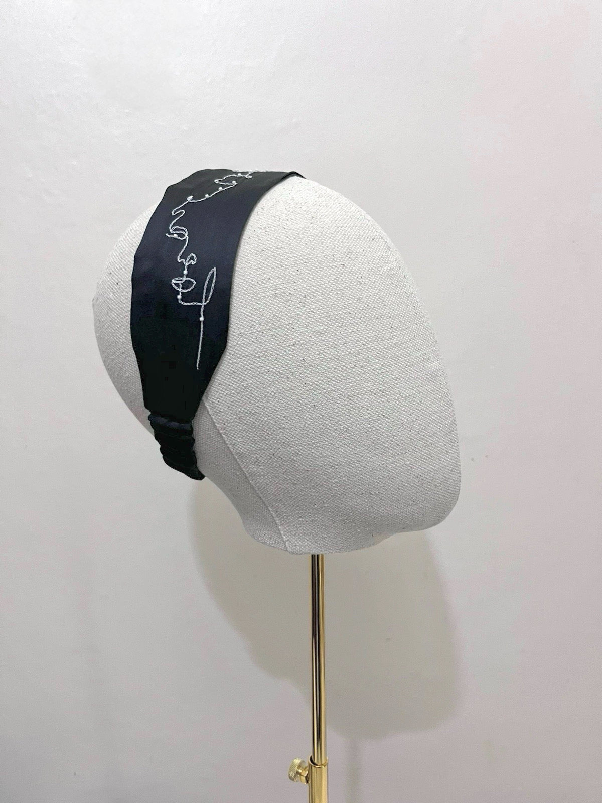 Black headband with white text on a gray mannequin head against a white background