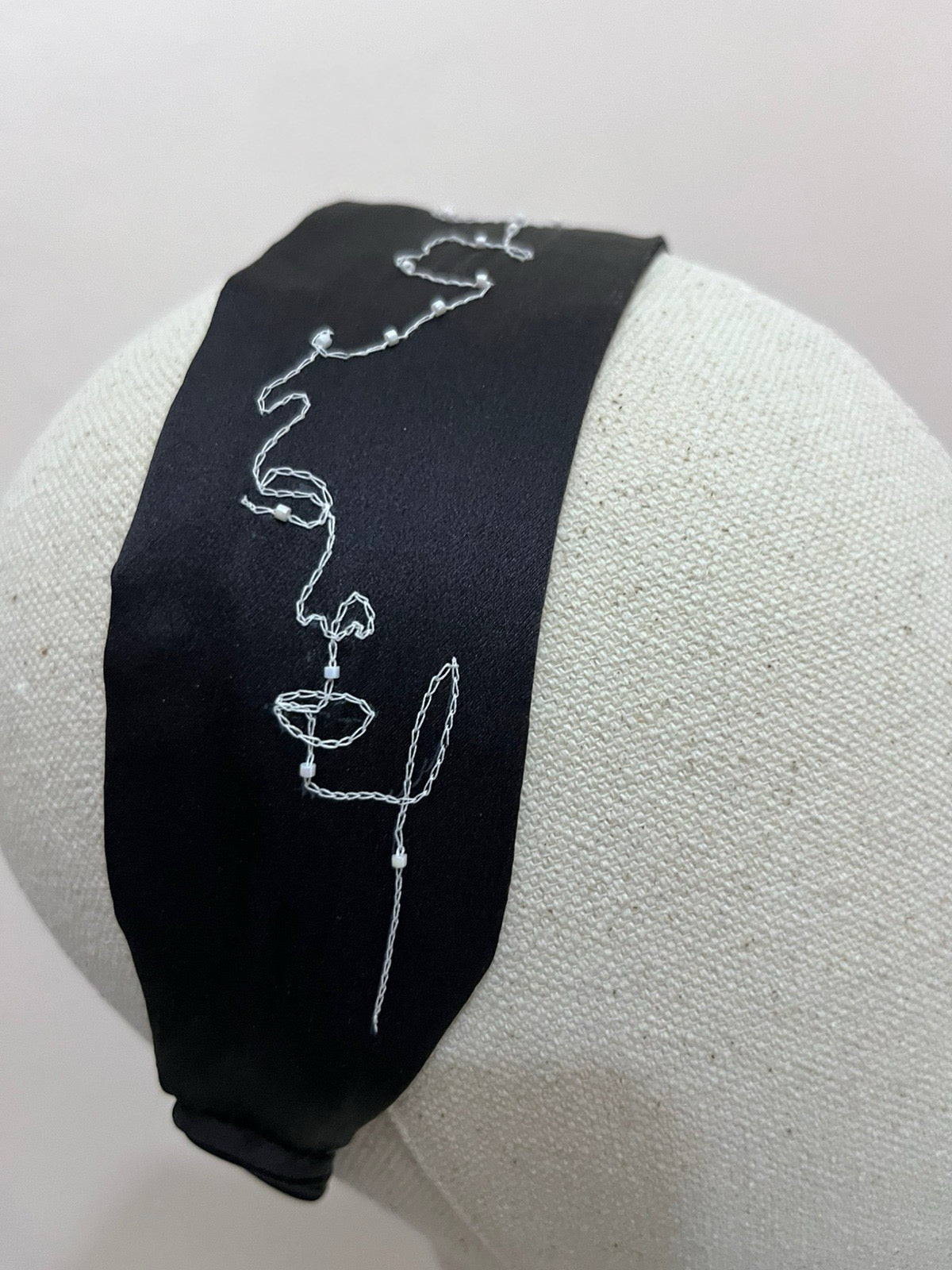 Black headband with white embroidery on a white stand.