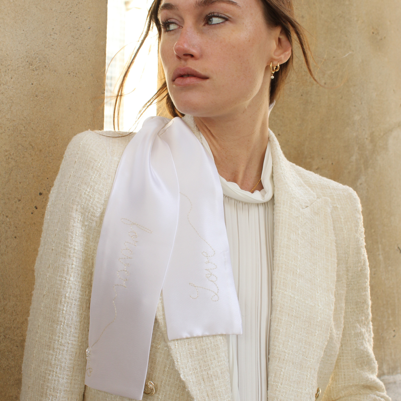 Woman wearing a beige textured jacket with a white hairband against a beige wall
