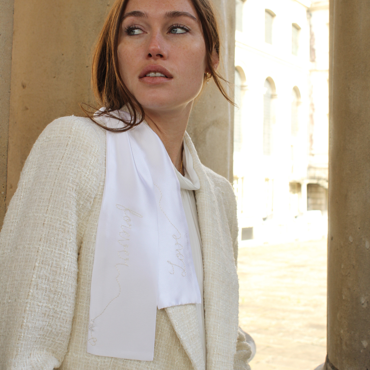 Woman wearing a light-colored outfit with a white shirt, standing against a neutral background.