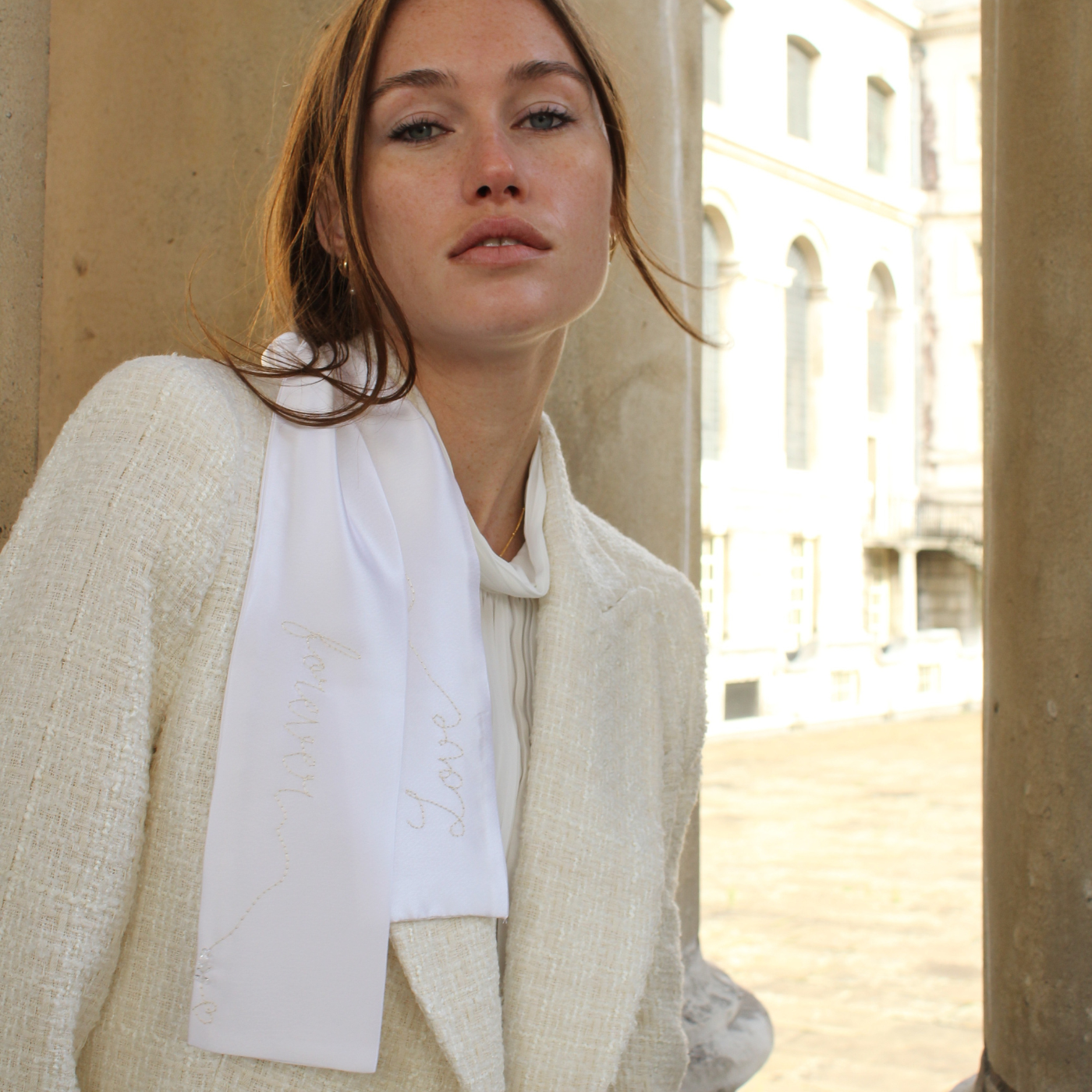 Woman wearing a white scarf and beige coat in an urban setting