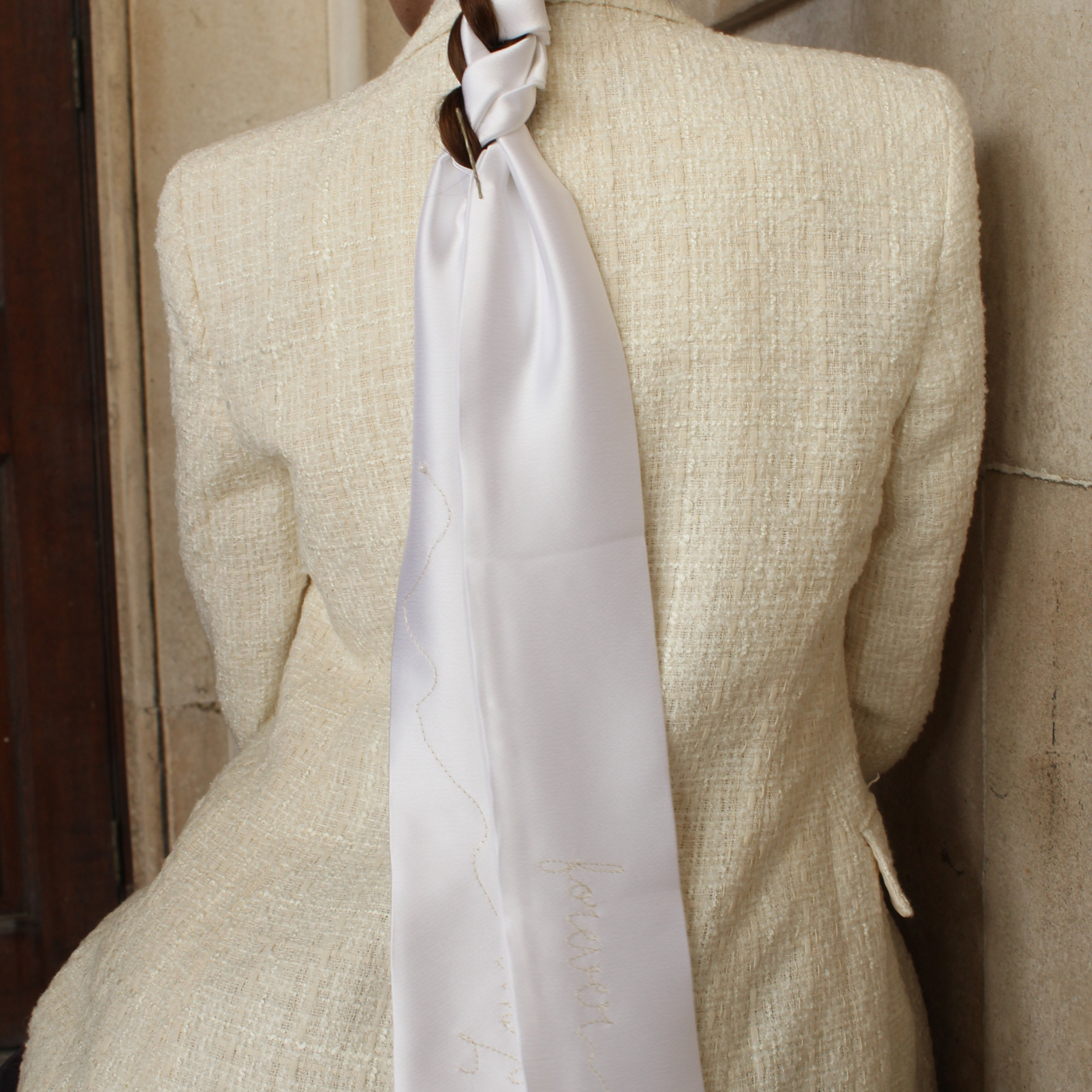Model wearing a beige suit with a white scarf breaded in her hair
