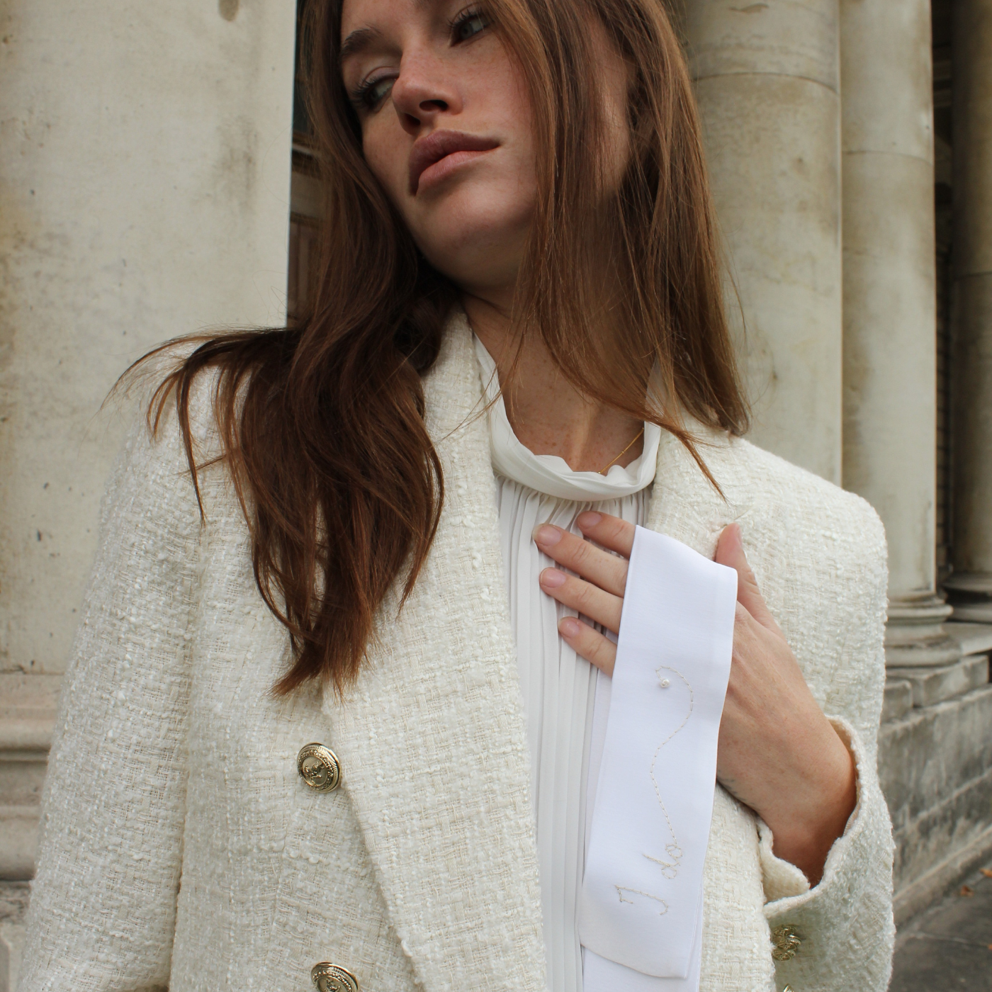 Woman in a white coat holding a hairband that saying I do, against a stone building background
