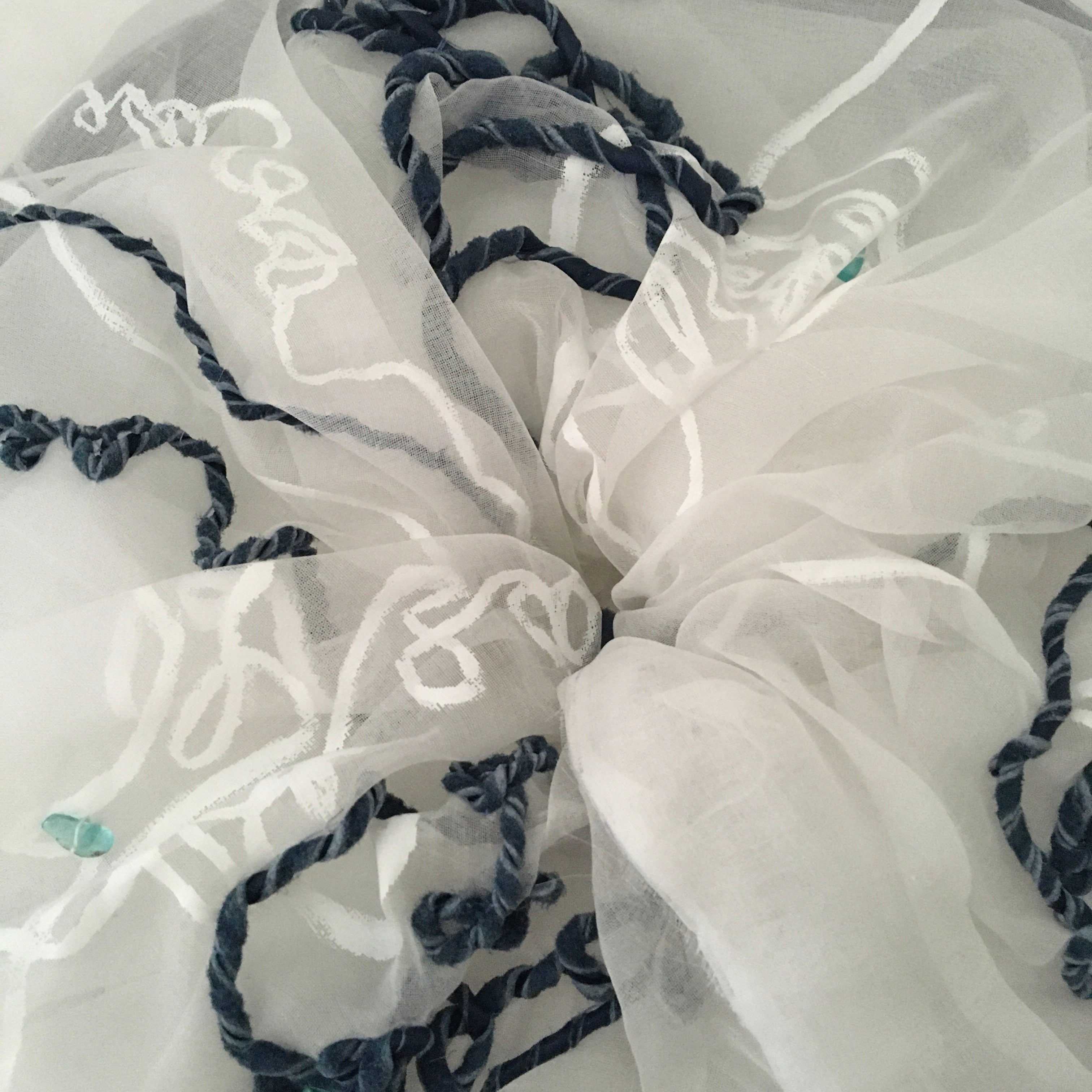 Close-up of a large scrunchy with white fabric with blue embroidery on a white background