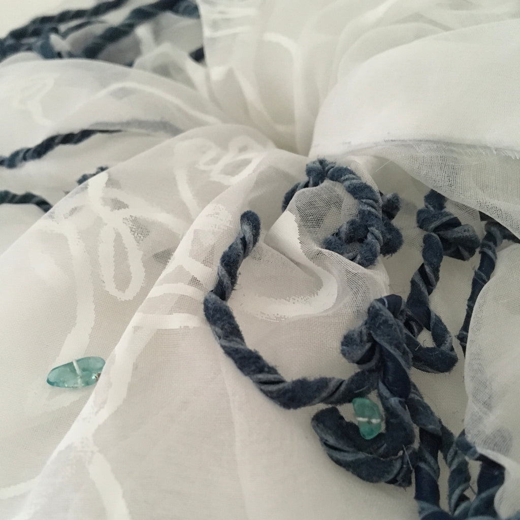 Close-up of a scrunchy with white fabric with blue embroidery and beads.