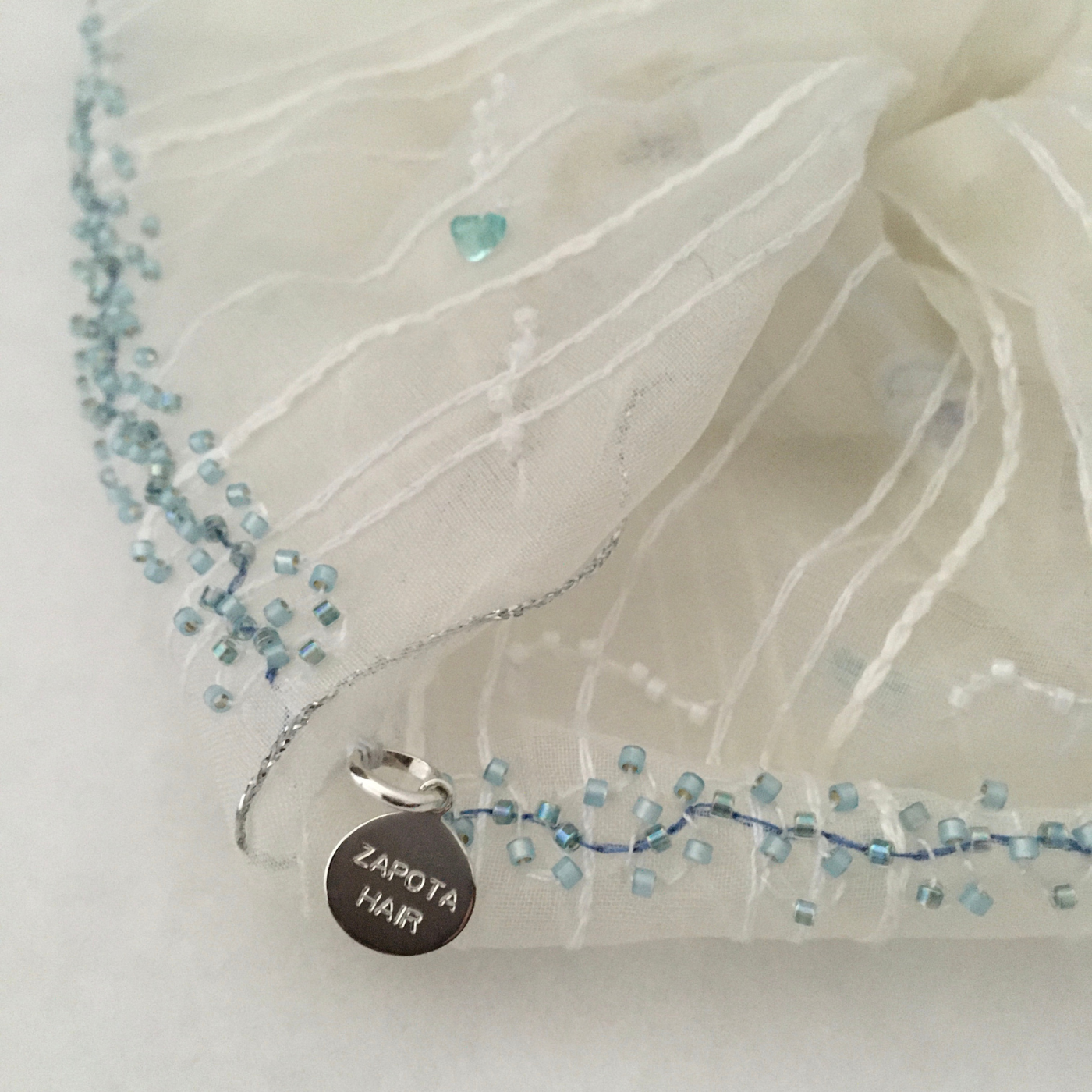 Scrunchy closeup with a round pendant labeled 'Zapota Hair' on a light fabric background