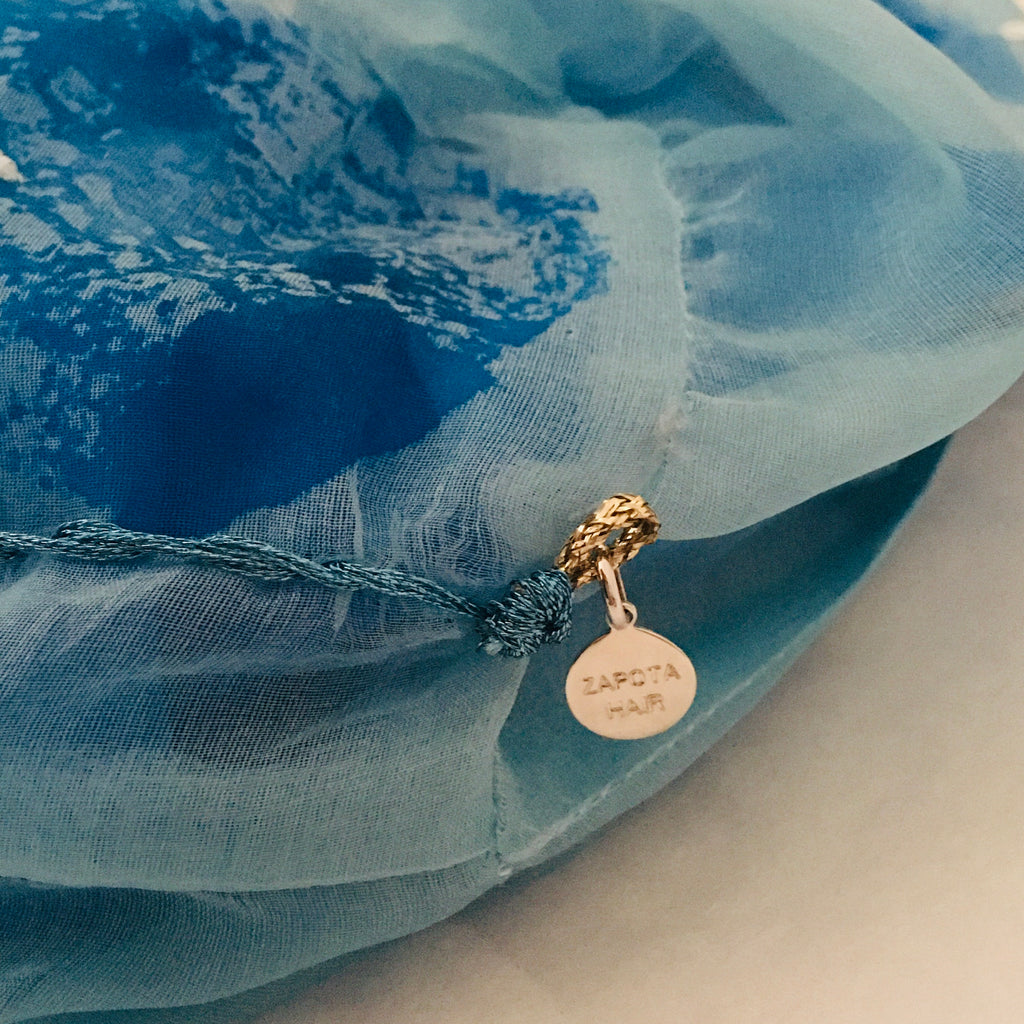 Close up of a large blue scrunchy with a silver charm on a blue fabric