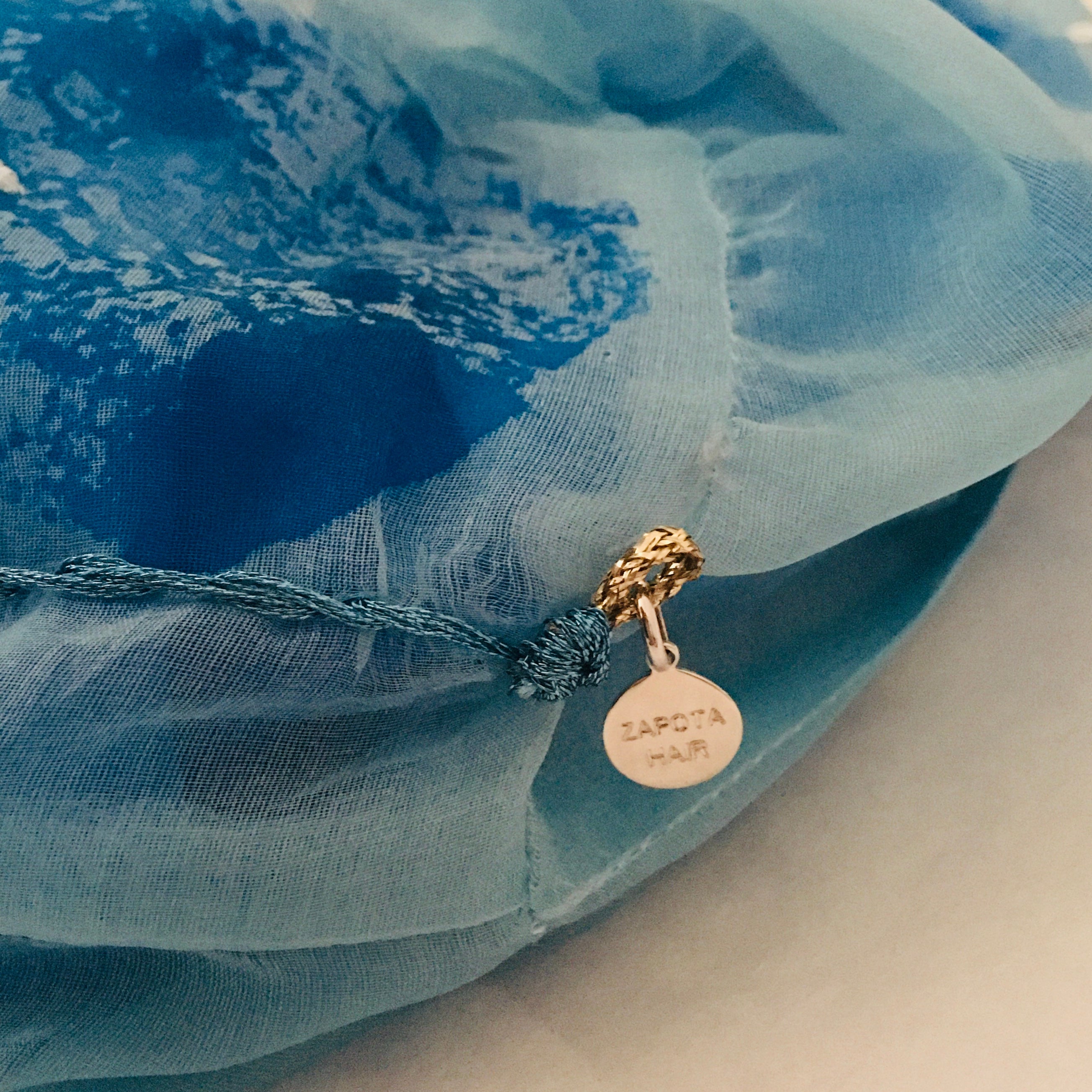 Close up of a large blue scrunchy with a silver charm on a blue fabric