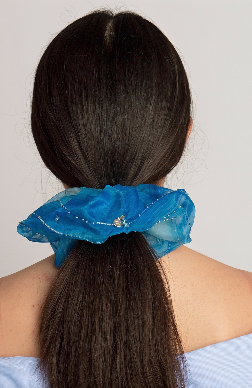 Blue scrunchie on a model's ponytail against a white background