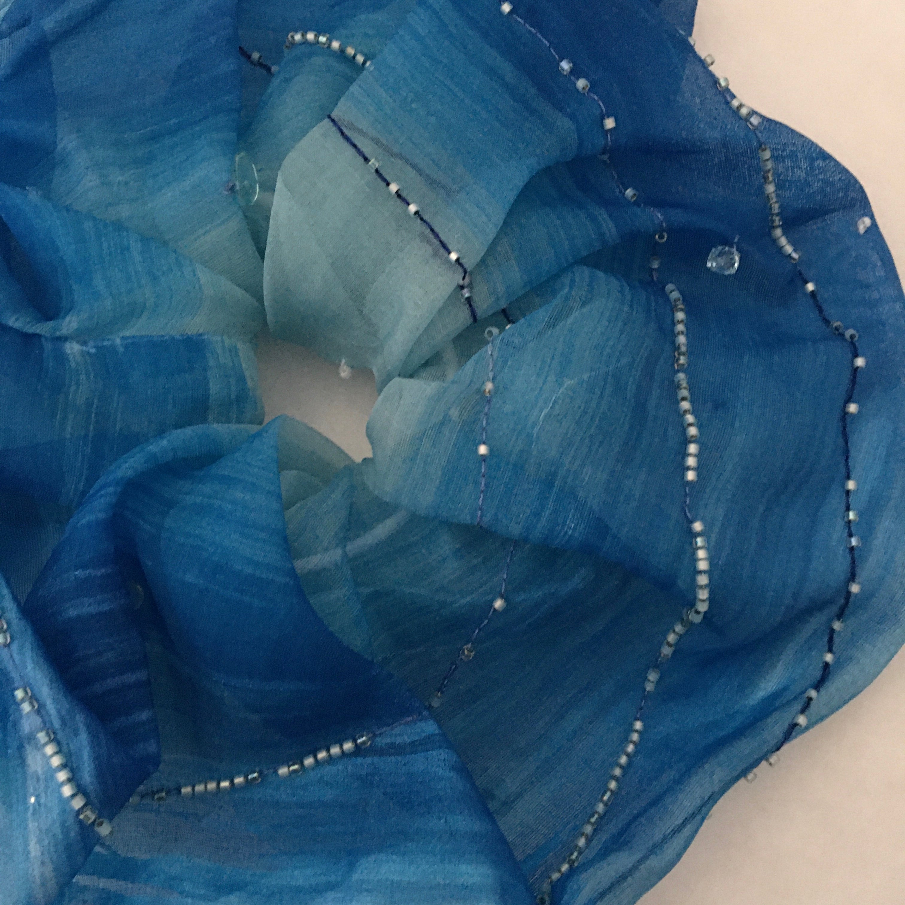 Oversize scrunchy with blue fabric with bead embellishments on a white background
