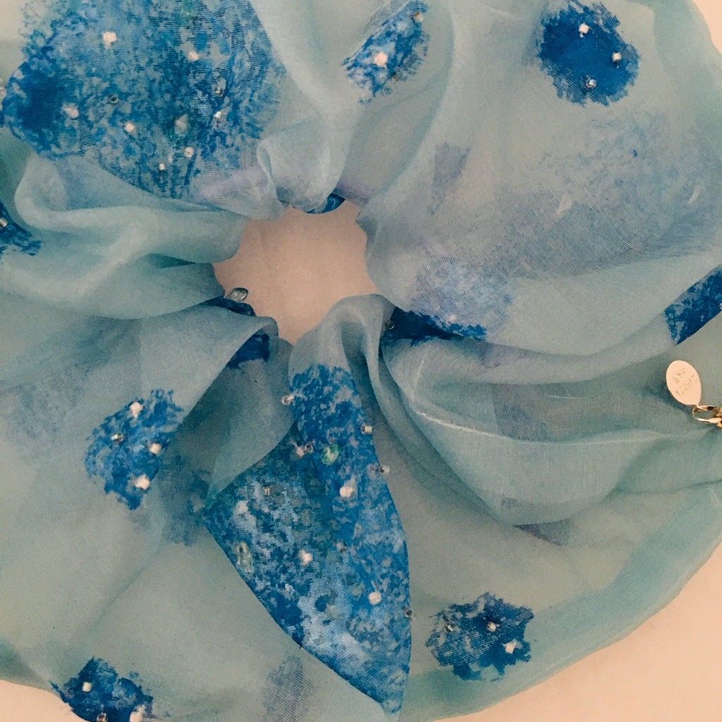 Close-up of a scrunchy with blue fabric with decorative elements on a white background