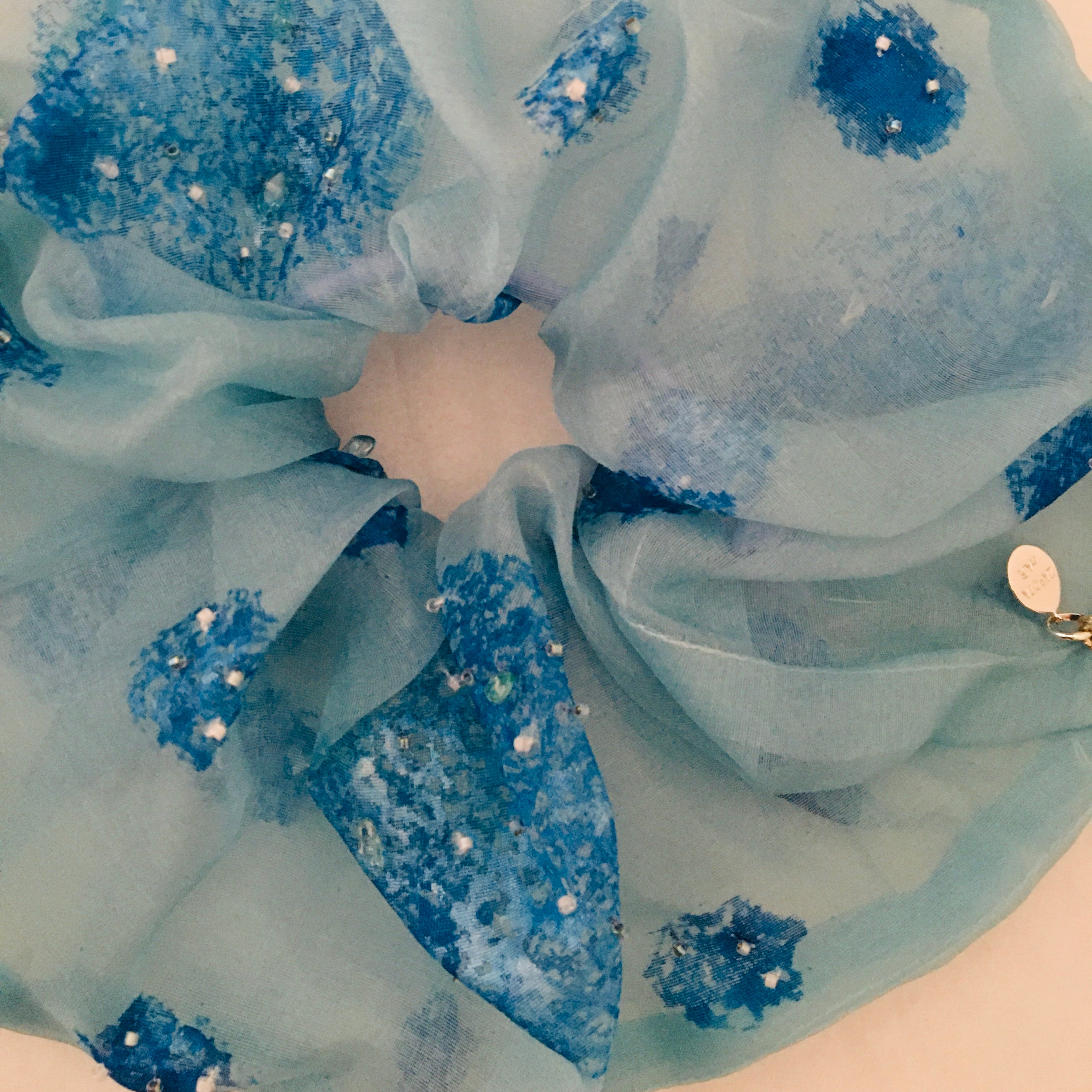 Close-up of a scrunchy with blue fabric with decorative elements on a white background