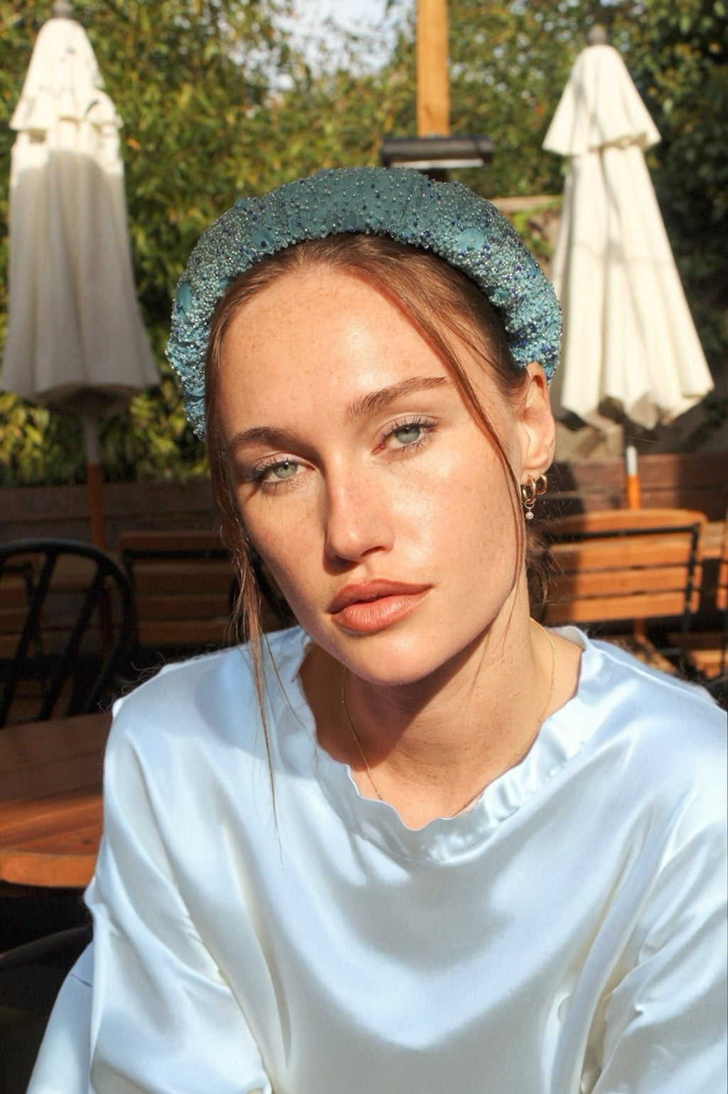 Woman wearing a light blue headband in an outdoor setting with tables and umbrellas.