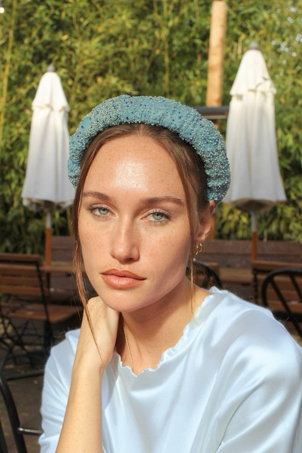 Woman wearing a textured headband in an outdoor setting with greenery and white umbrellas.