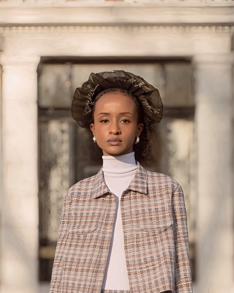 Model wearing a textured hat and patterned coat in front of classical architecture