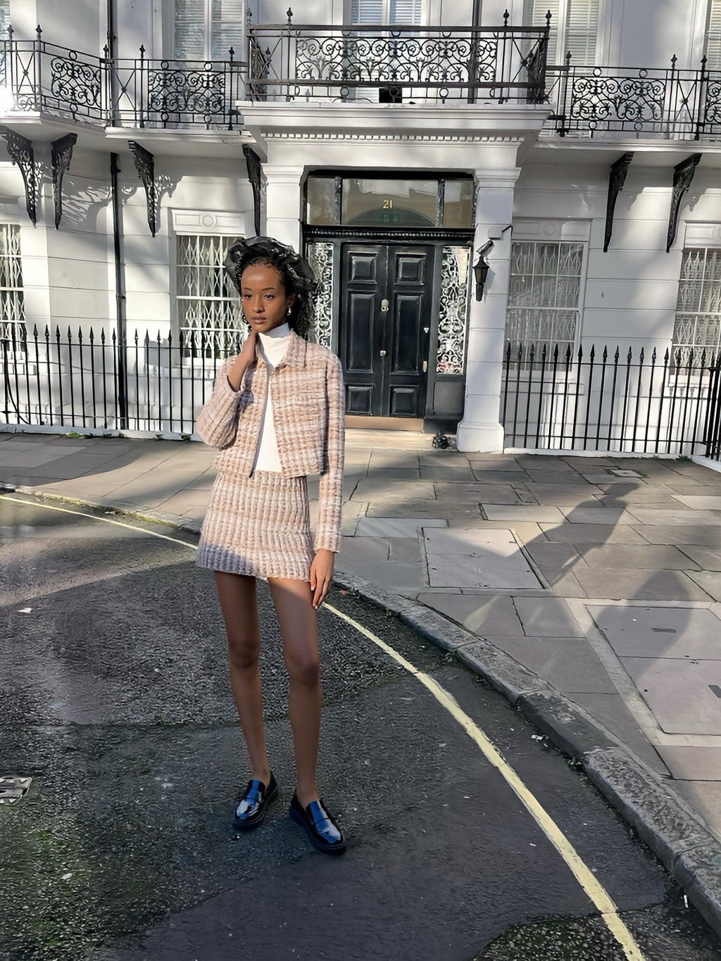 Woman in a checkered outfit standing on a street with a building in the background