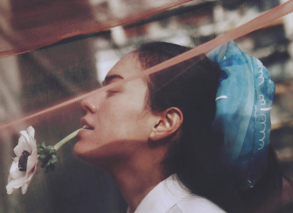 Model holding a white flower with a blurred background and wearing a large blue scrunchy