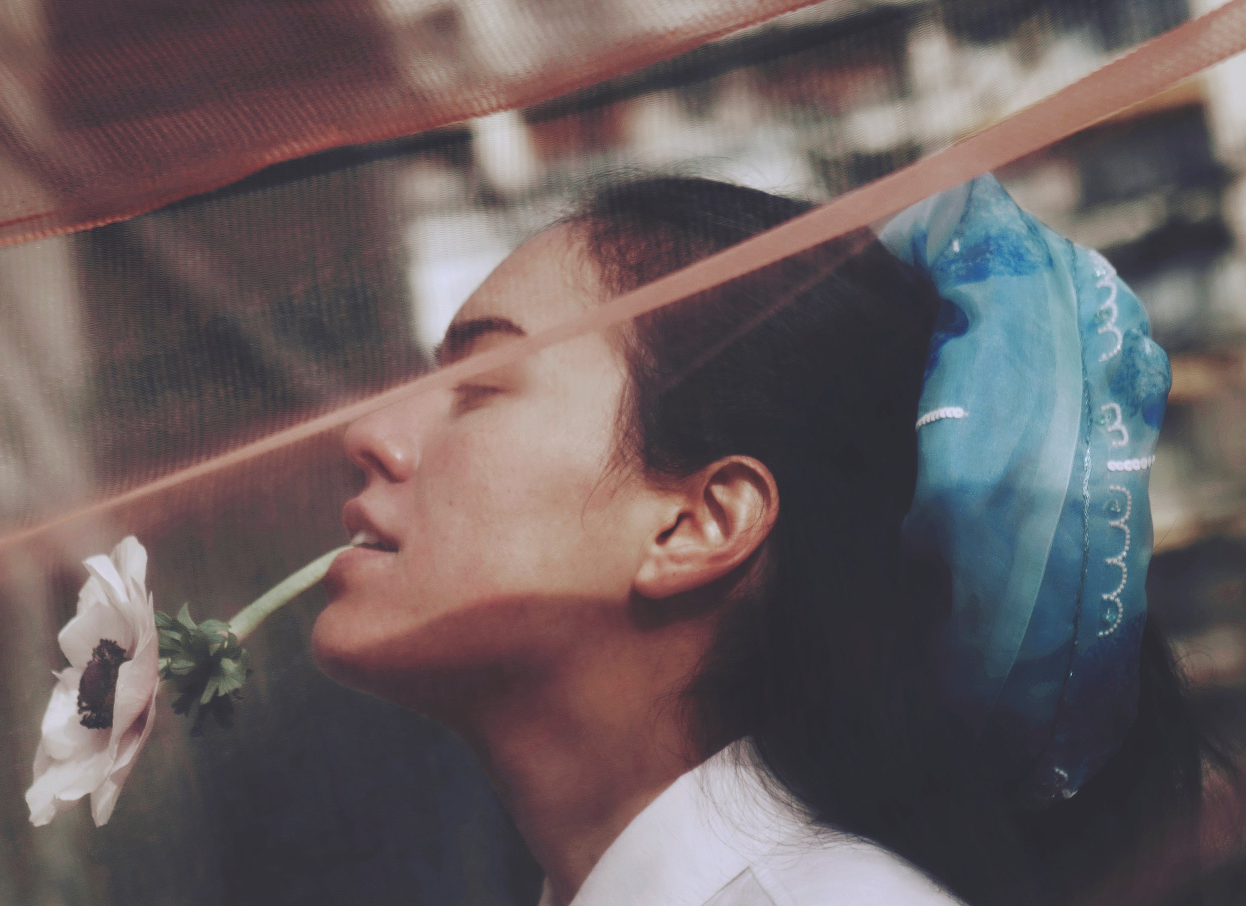 Model holding a white flower with a blurred background and wearing a large blue scrunchy