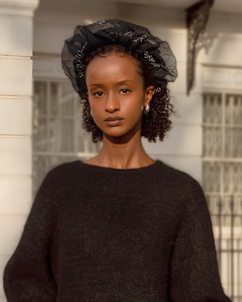 A model wearing a black headband and sweater against a neutral background