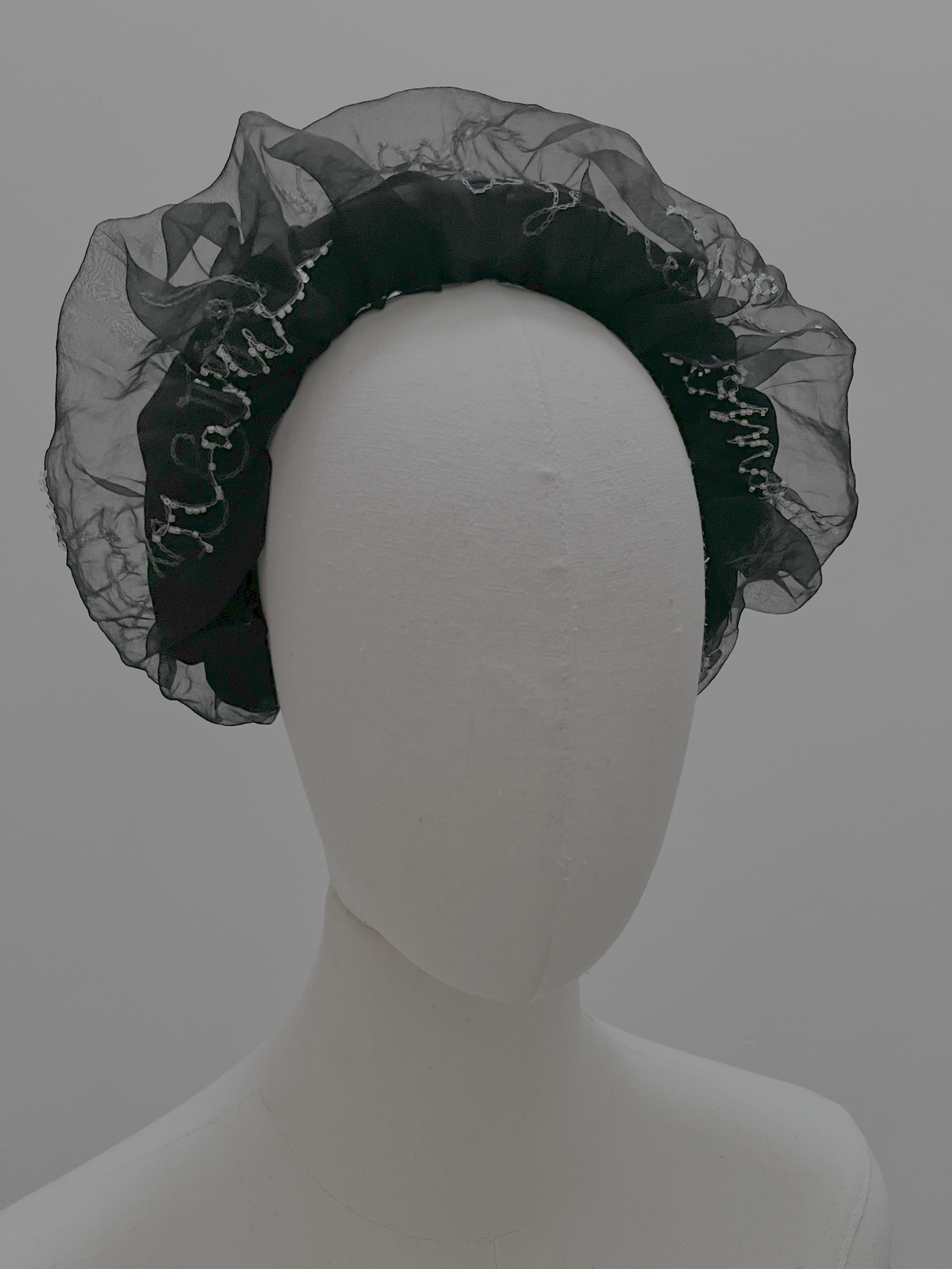 A black sheer organza headband with delicate bead trim, displayed on a white mannequin head against a light gray background.