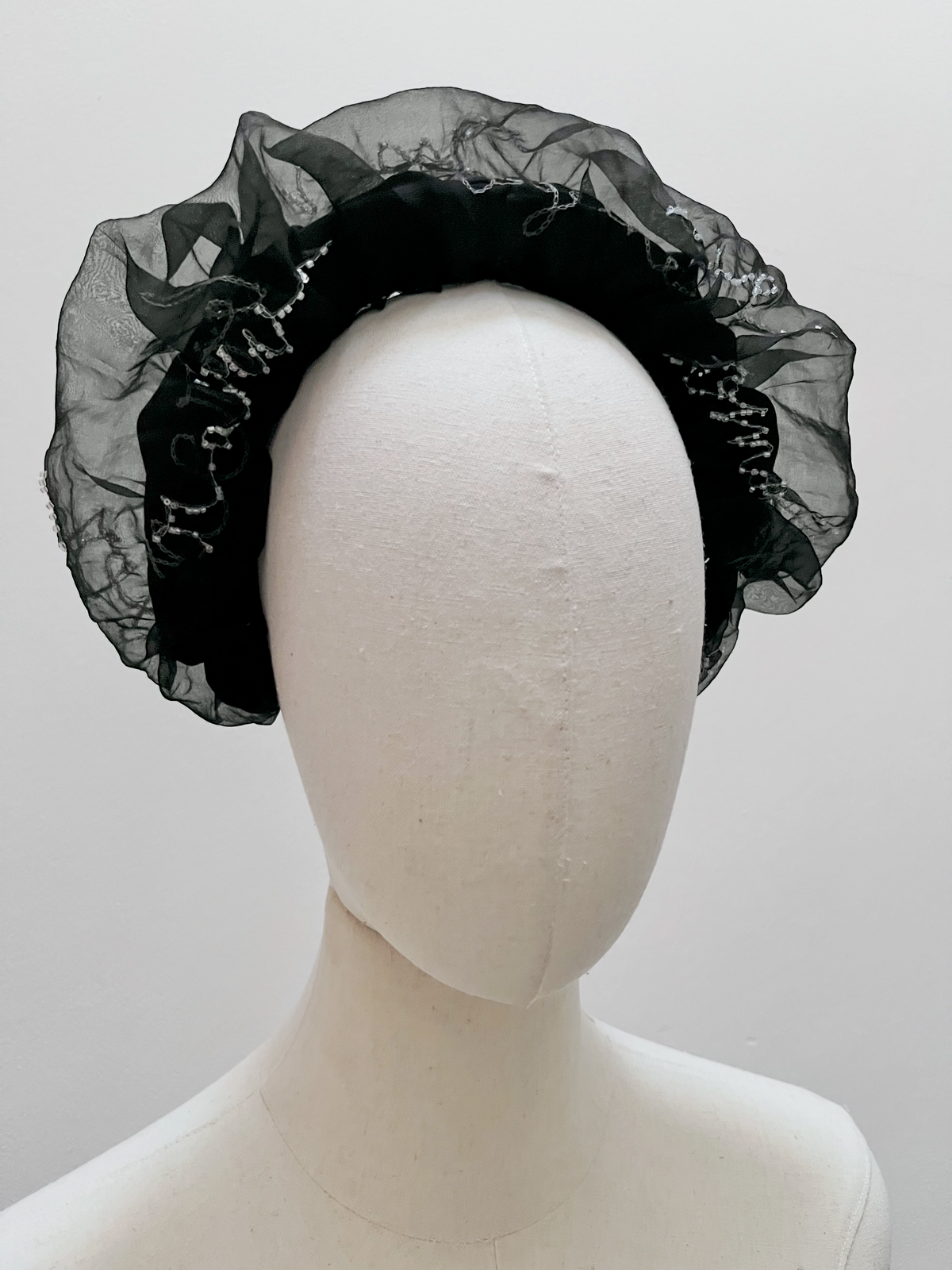 A black sheer organza headband with delicate bead trim, displayed on a white mannequin head against a light gray background.