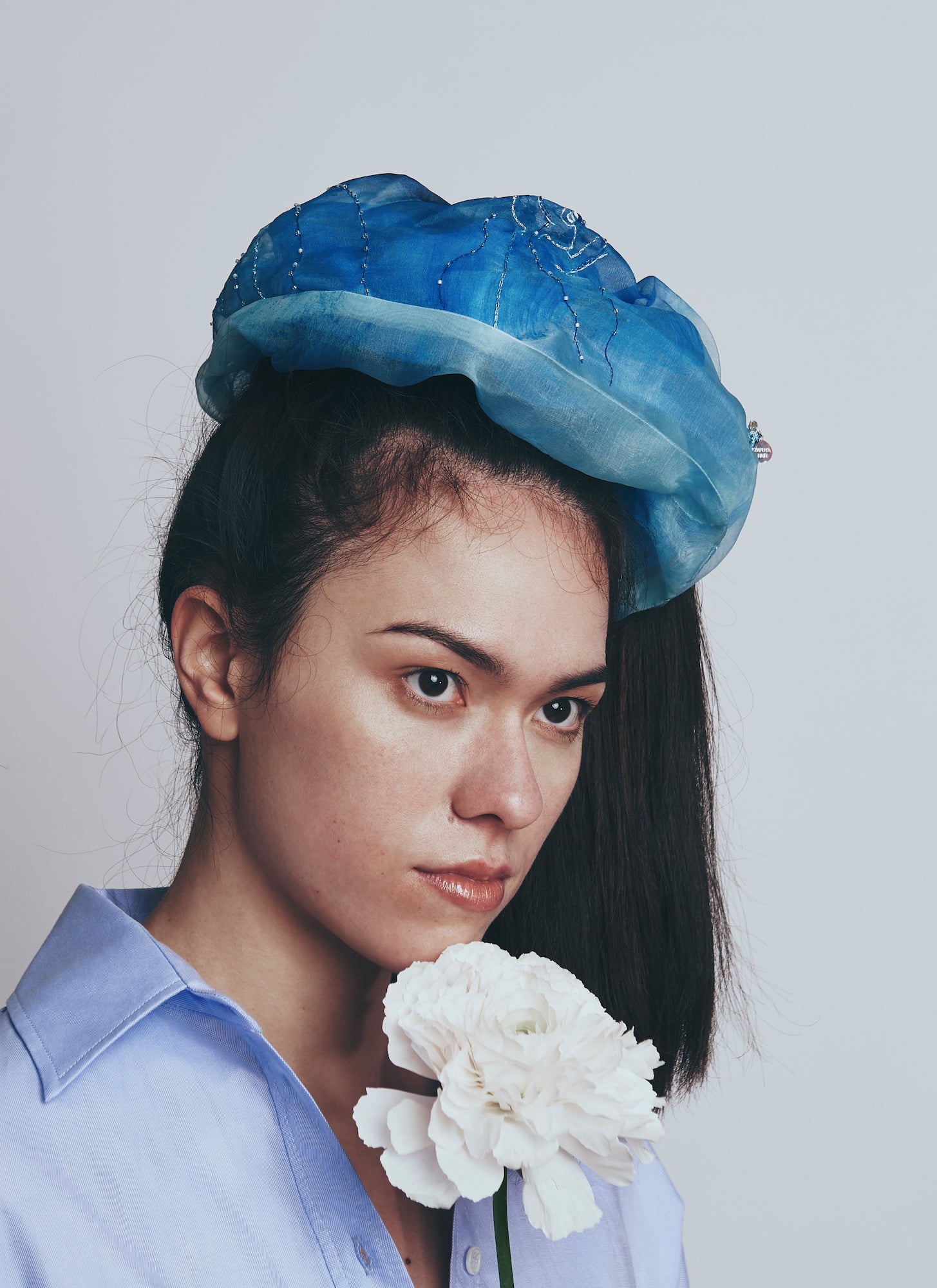 Model wearing a blue denim scrunchy and holding a white flower against a plain backgrounk