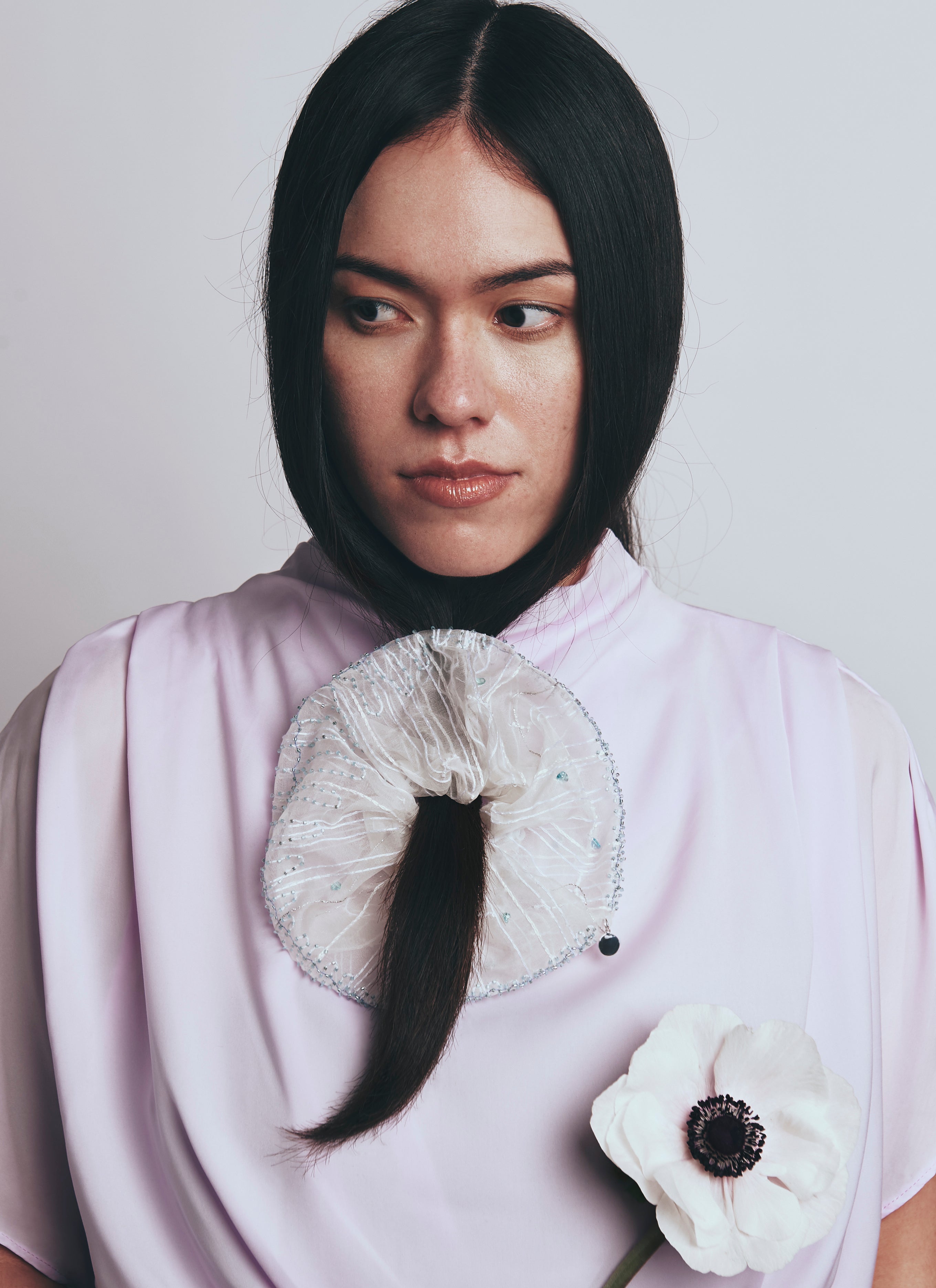Person wearing a white garment with a large scrunchy with embroidery and a white flower accessory.