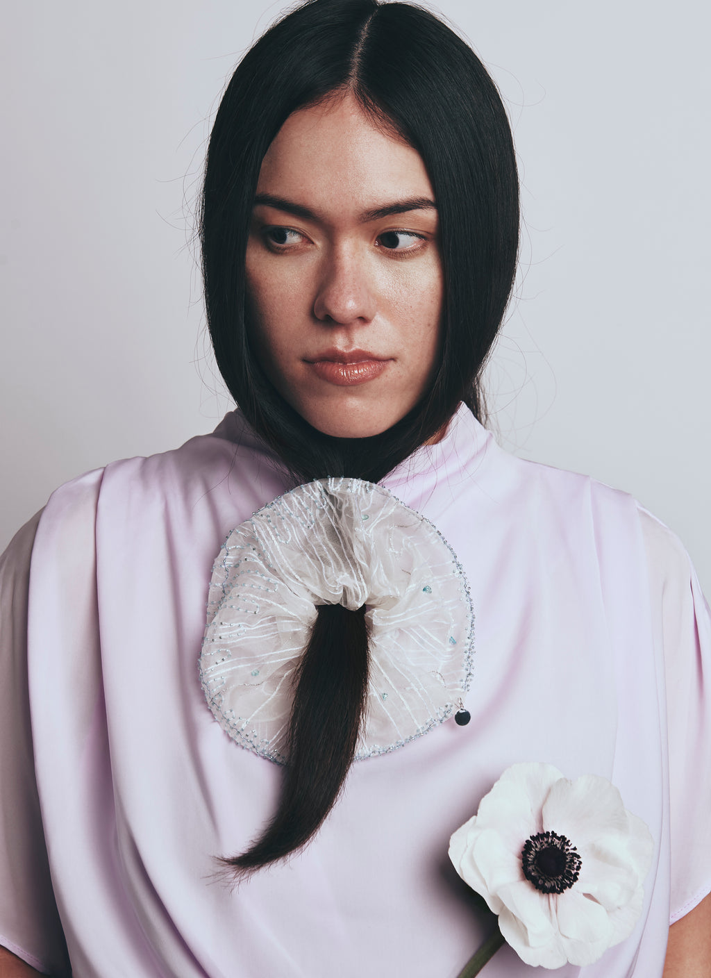 Person wearing a white garment with a large scrunchy with embroidery and a white flower accessory.