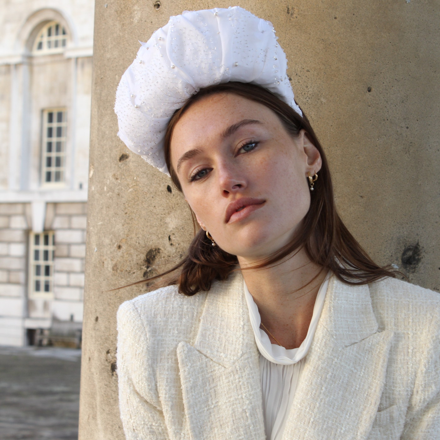 Woman wearing a white hat and coat against a stone wall.