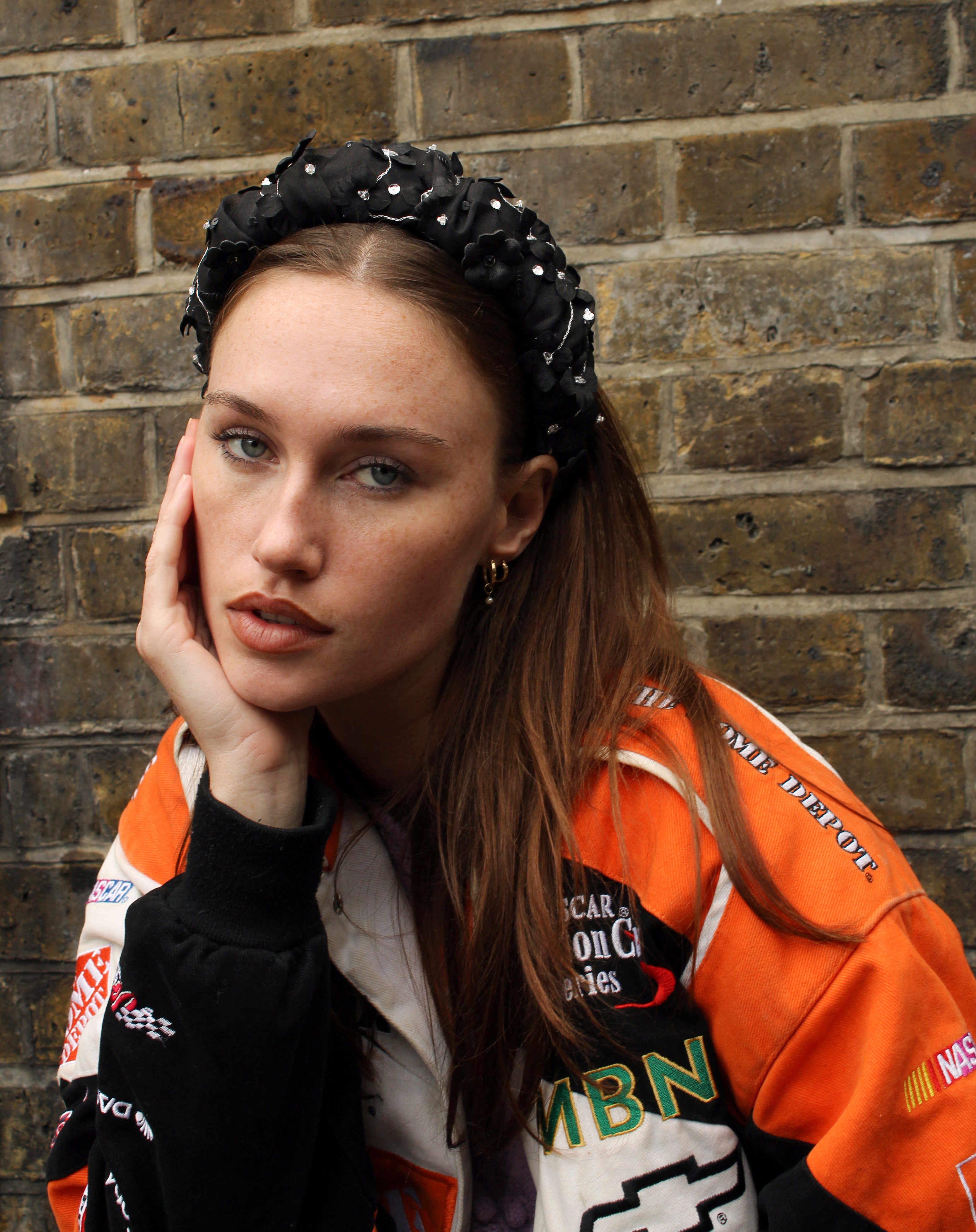 Woman wearing a black handmade headband and colourful jacket with logos against a brick wall