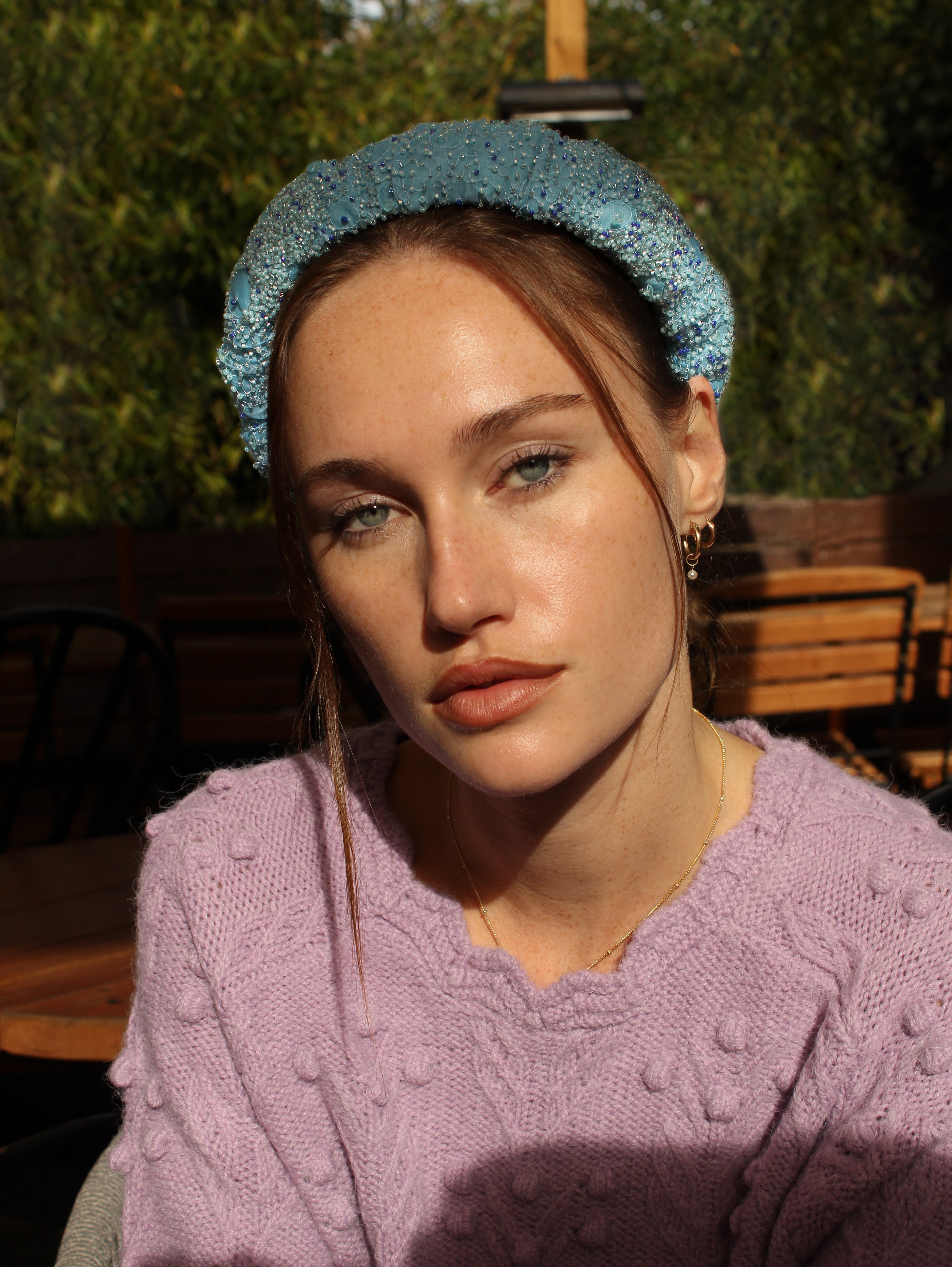 Woman wearing a blue headband with beads and pink sweater outdoors