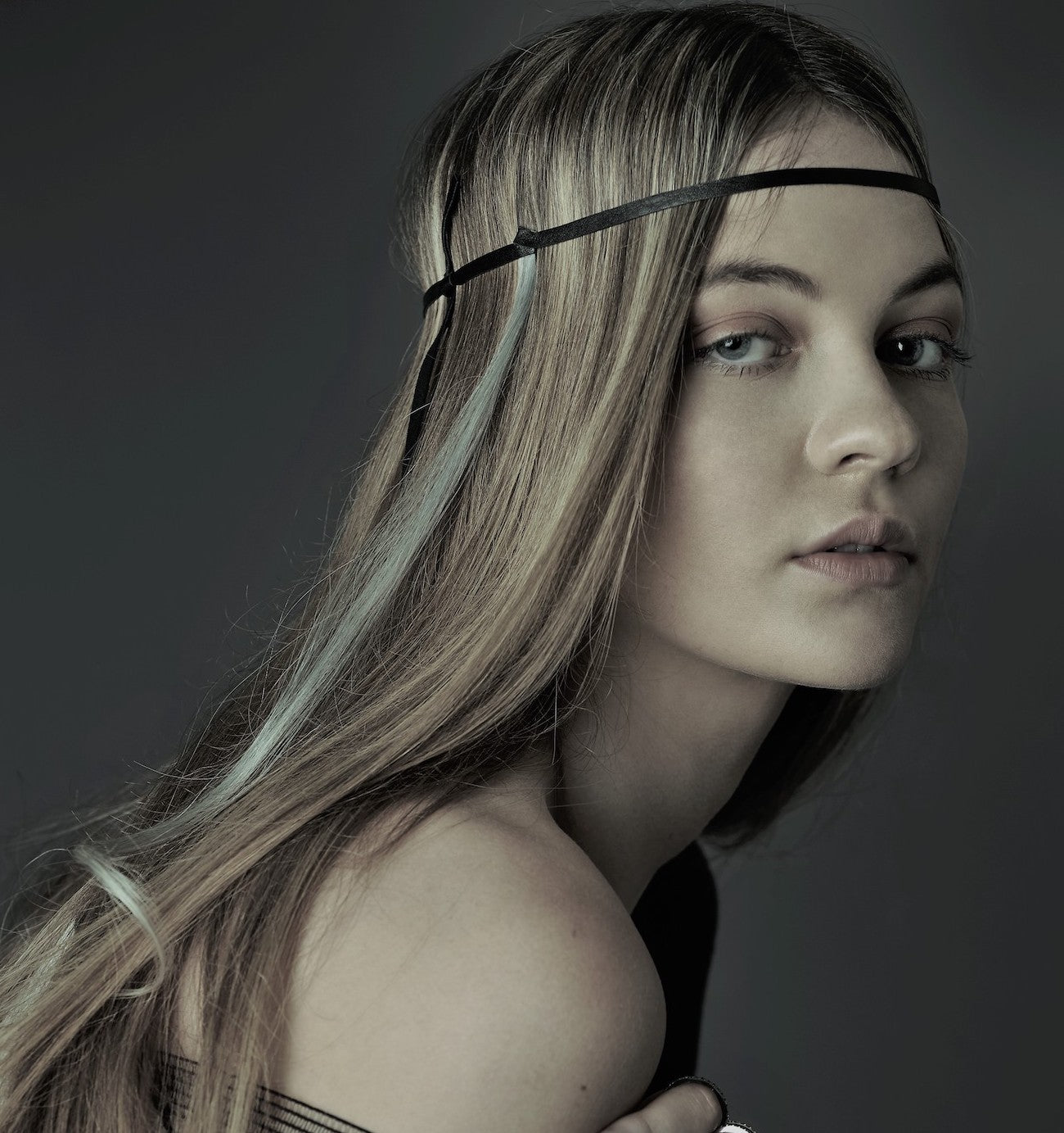 Model with long hair wearing a headband against a dark background