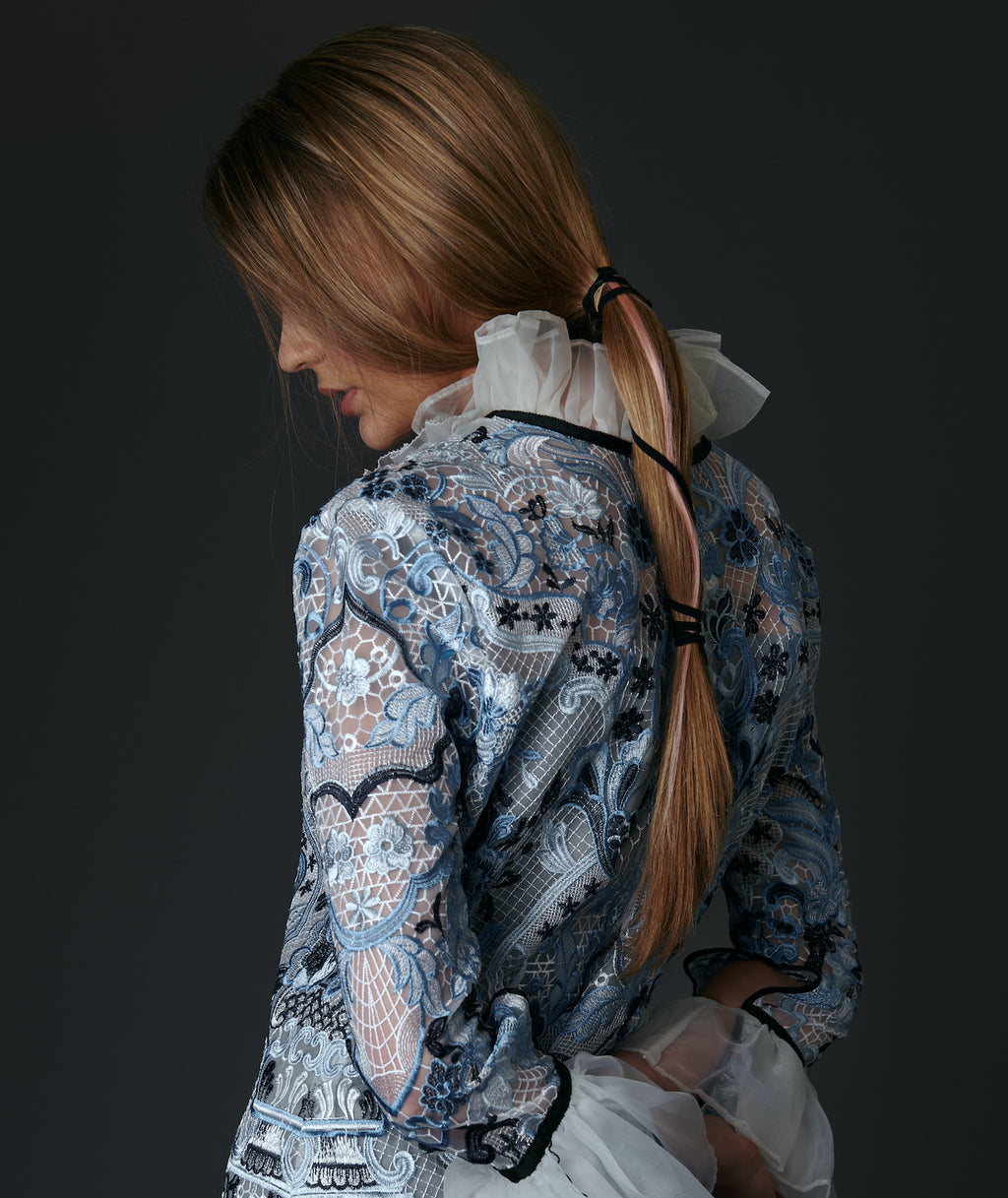 Model wearing a detailed floral blouse against a dark background