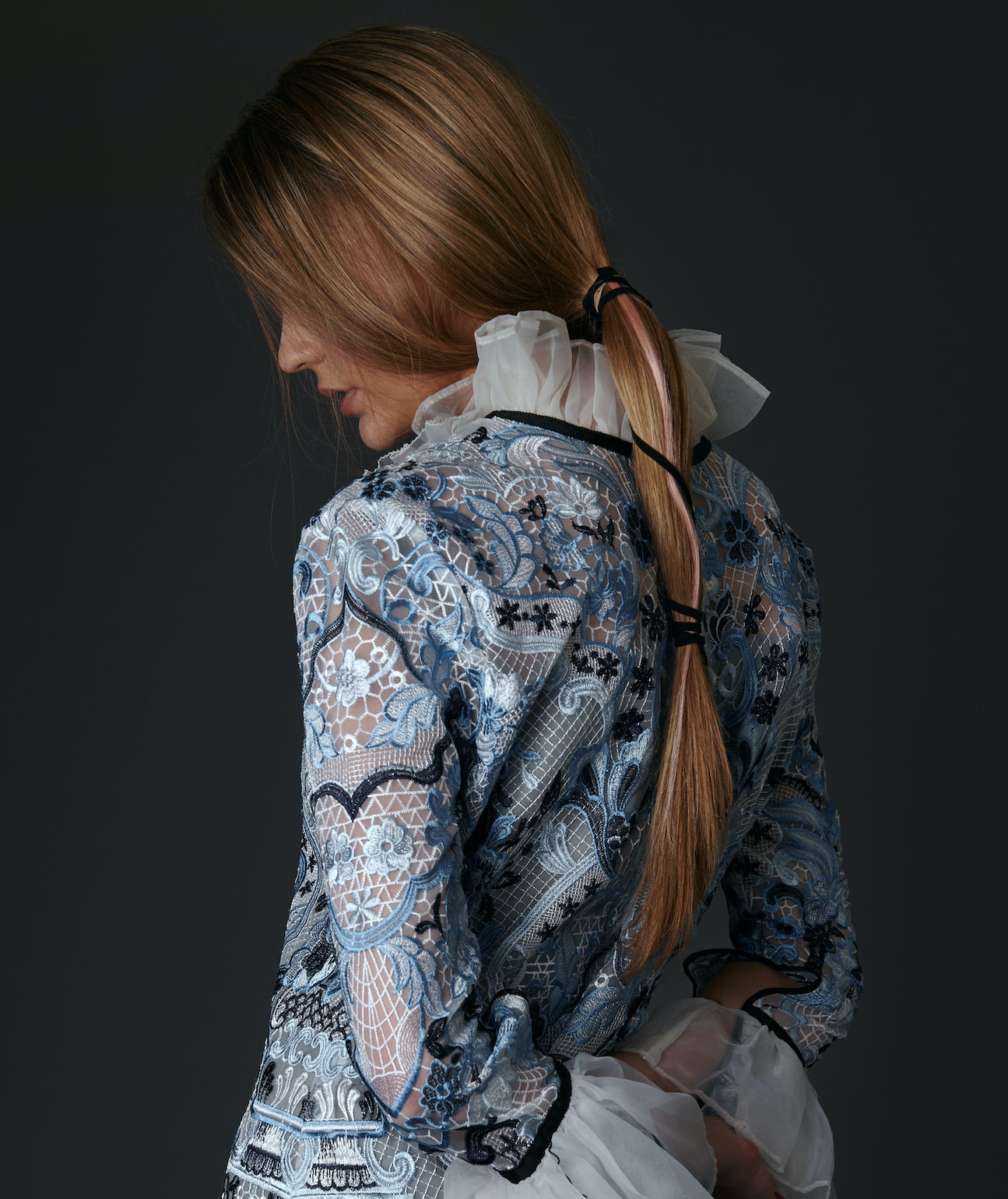 Model wearing a detailed floral blouse against a dark background