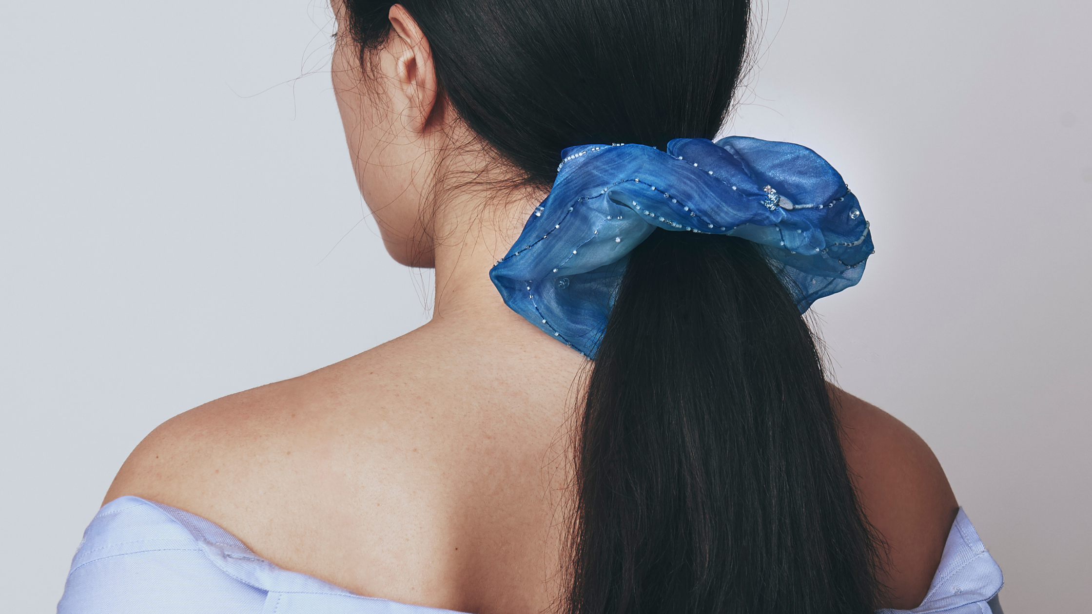 A model with black hair and a blue scrunchie in their hair against a plain background